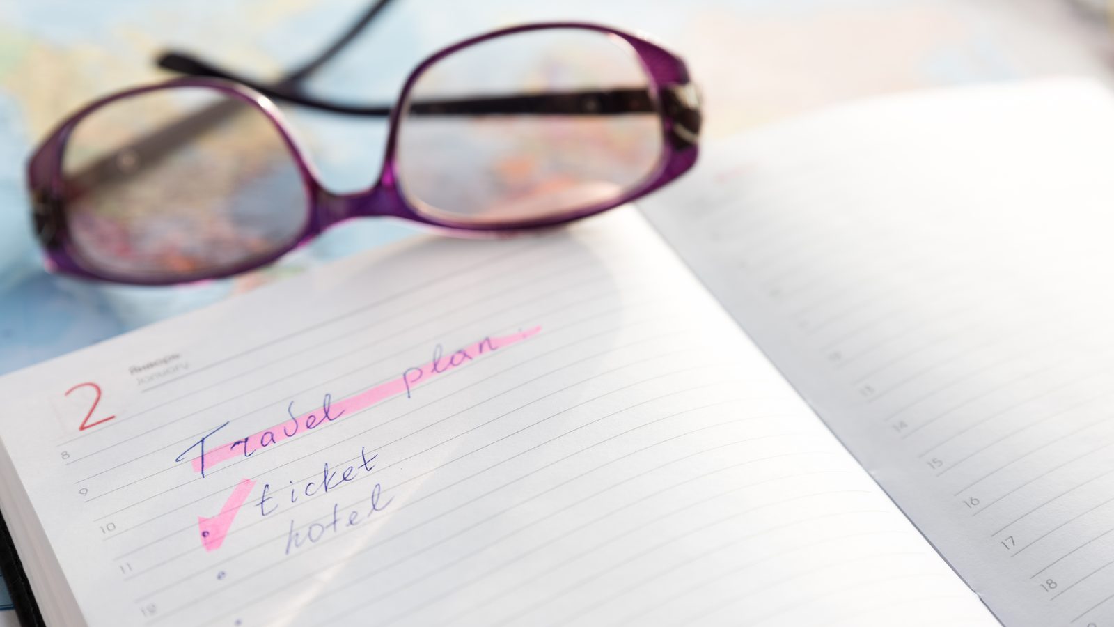 A handwritten travel-plan checklist in a notebook, with reading glasses resting on the page