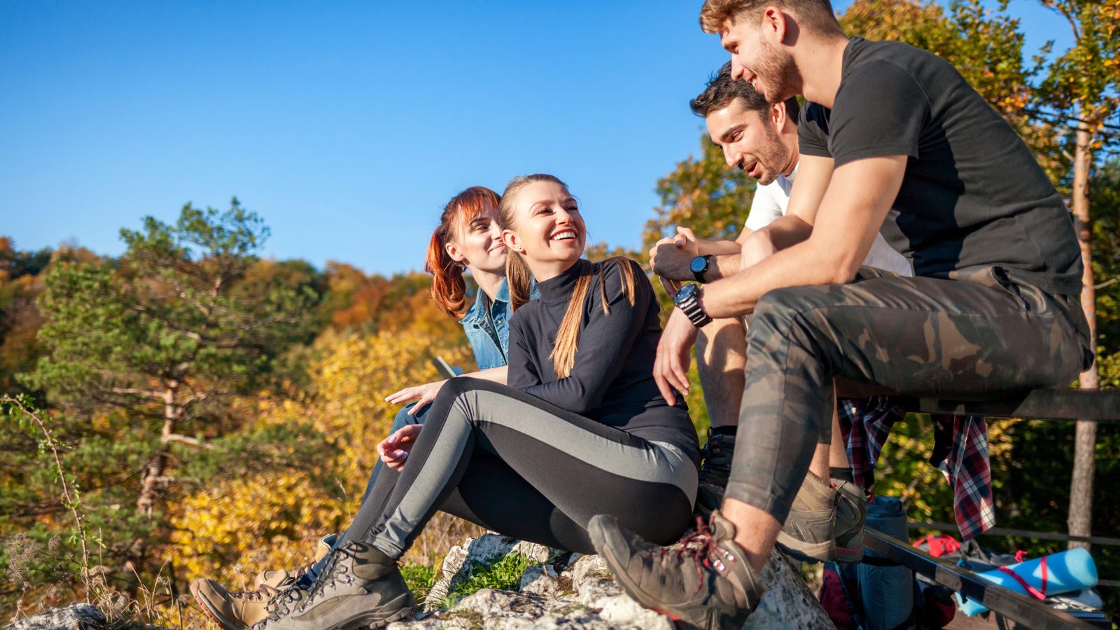 Four walkers with rucksacks sitting on rocks and laughing during a break on a wooded hillside