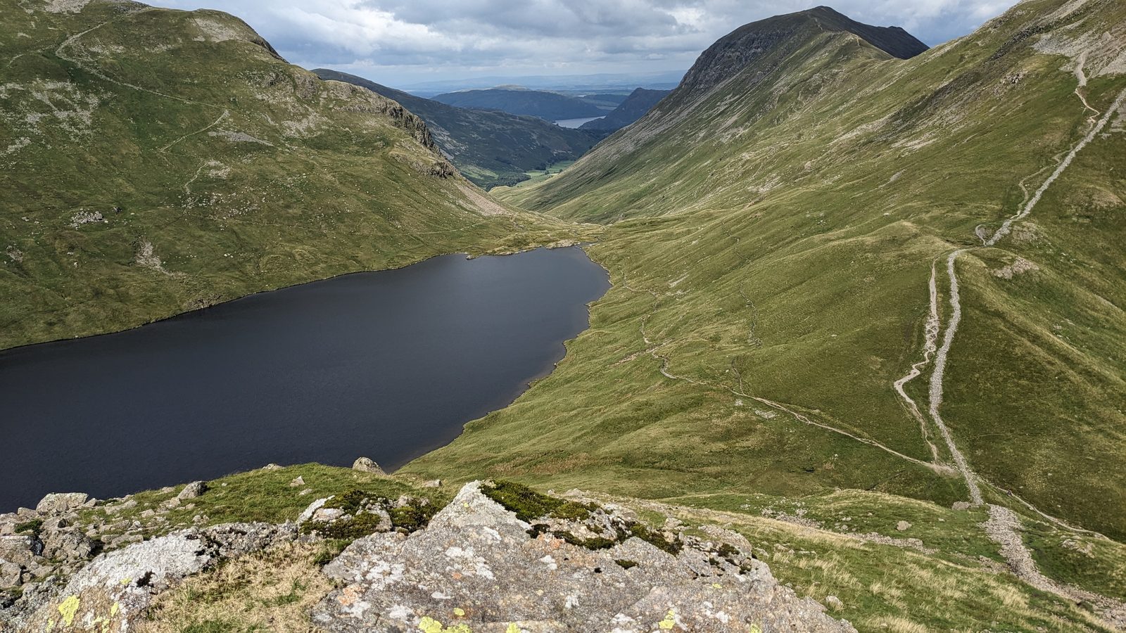 A mountain tarn in a rocky corrie with paths running above it, on the Grasmere to Patterdale stage