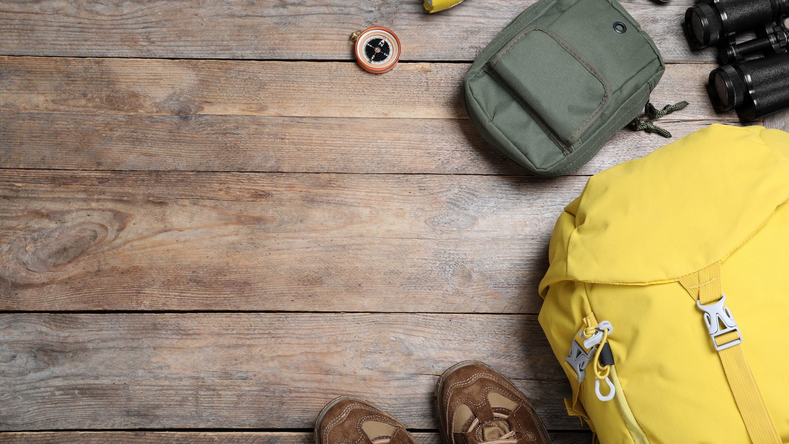 Walking boots, a yellow daysack, a compass, binoculars and a head torch laid out on a wooden table